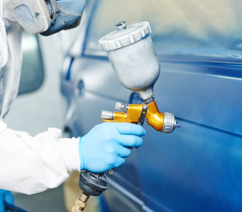 automobile repairman painter hand in protective glove with airbrush pulverizer painting car body in paint chamber